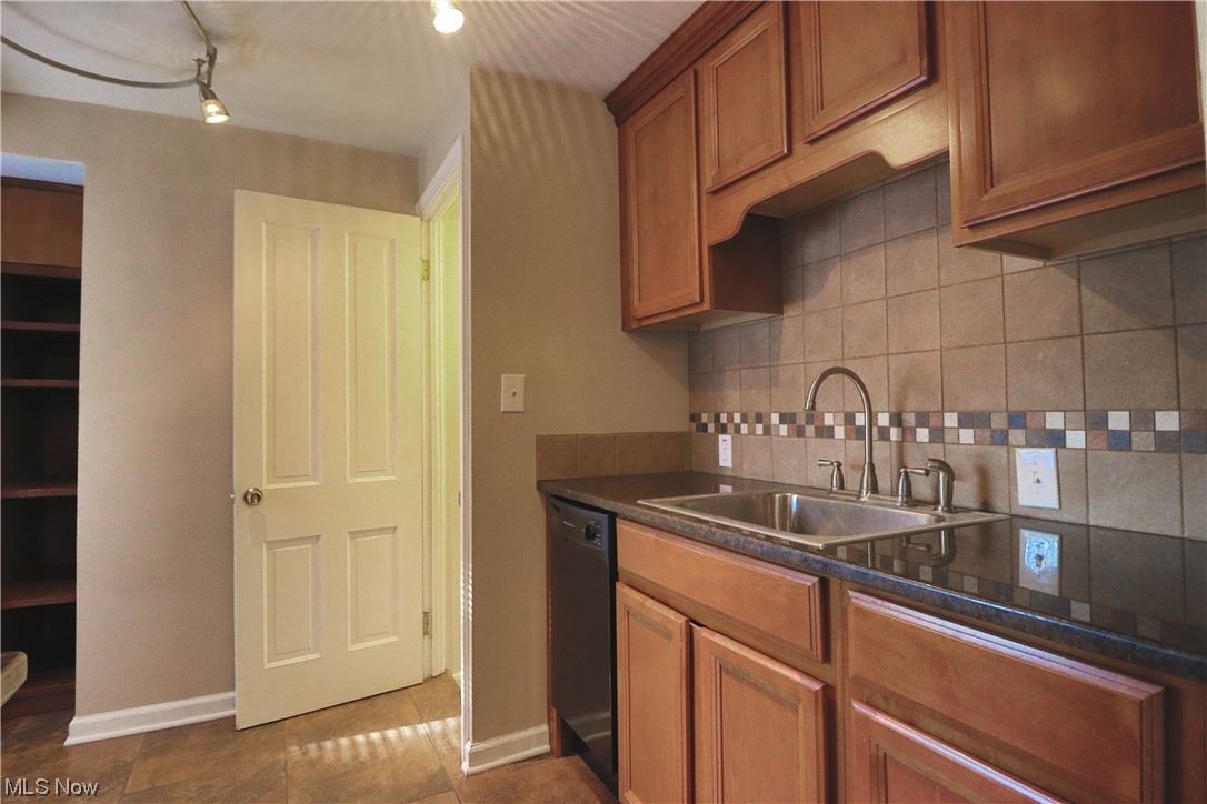 1351 Dill Road Cleveland, OH 44121 - Photo 9 of 24 Kitchen with black dishwasher, backsplash, dark countertops, brown cabinets, track lighting, and light tile floors