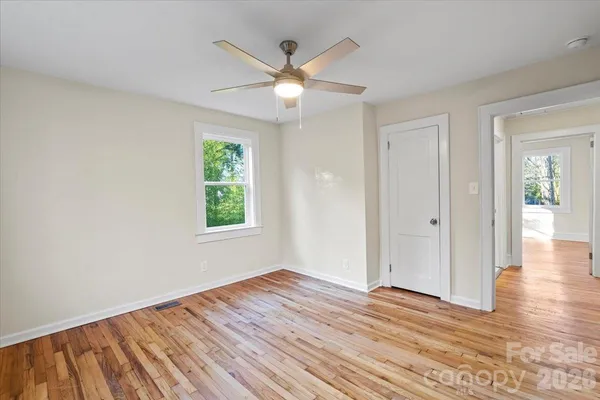 an empty room with wooden floor chandelier fan and windows