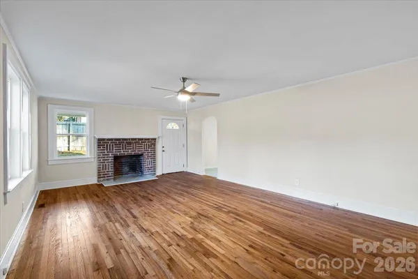 an empty room with wooden floor fireplace and windows