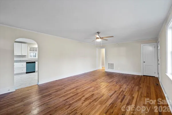 a view of empty room with wooden floor and kitchen view