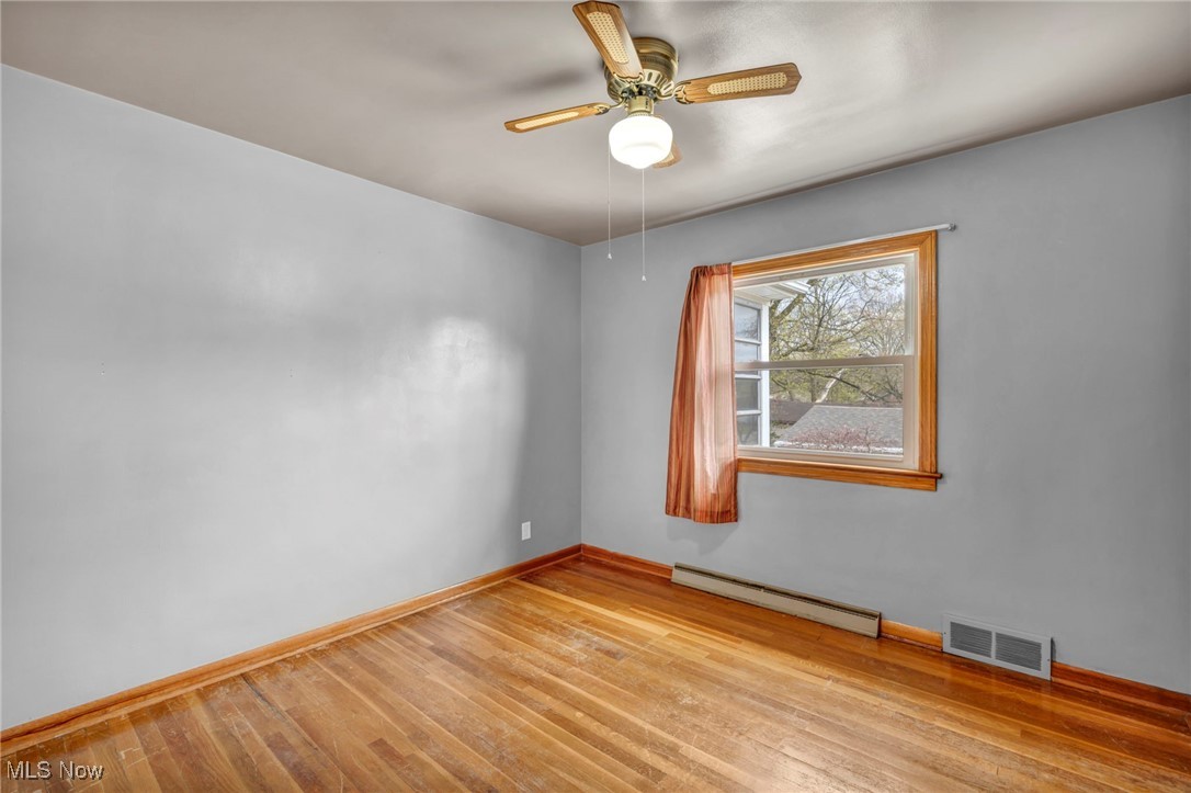 367 High Grove Boulevard Akron, OH 44312 - Photo 19 of 46 Spare room with wood finished floors, visible vents, a ceiling fan, a baseboard heating unit, and baseboards