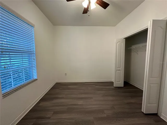 an empty room with wooden floor chandelier fan and windows