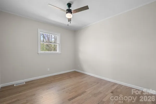 an empty room with wooden floor ceiling fan and window