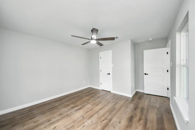a view of an empty room with wooden floor and a ceiling fan