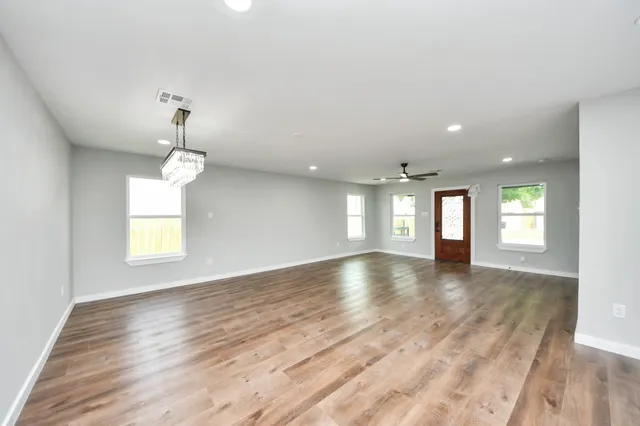 a view of an empty room and kitchen with sink wooden floor and windows