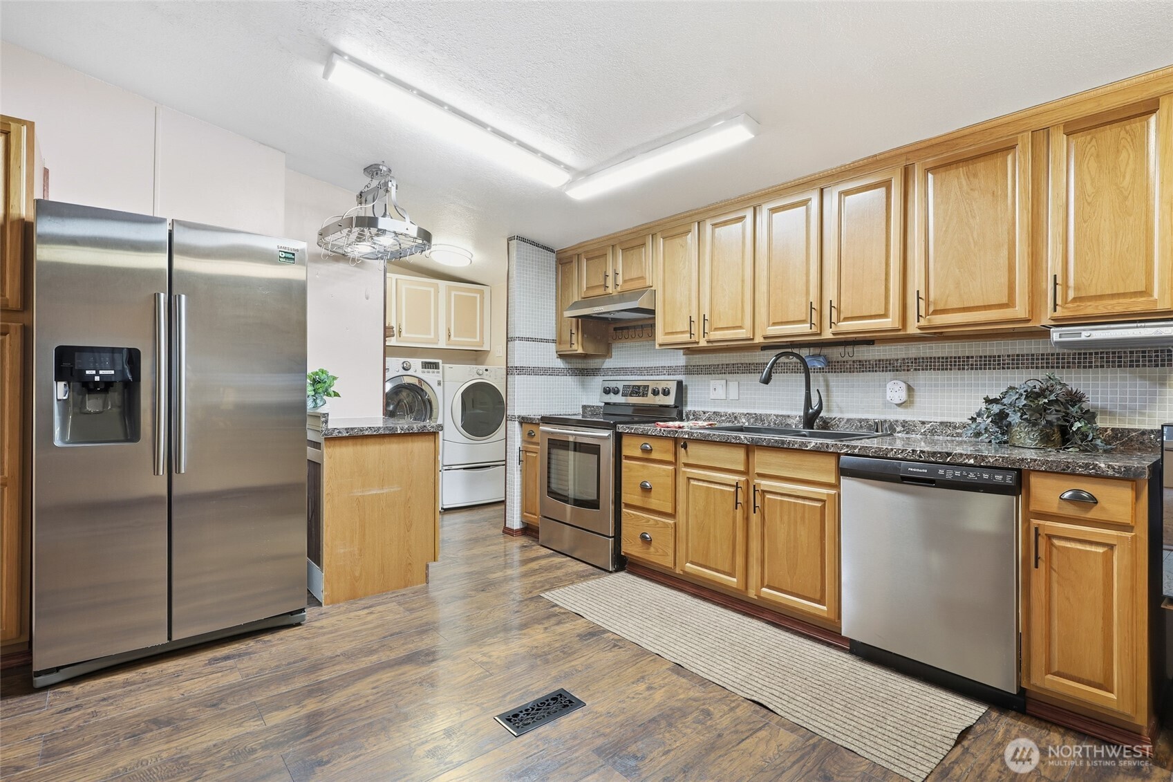 17340 Sargent Road Southwest, Unit 54 Rochester, WA 98579 - Photo 2 of 30 a kitchen with granite countertop a refrigerator a sink dishwasher and white cabinets with wooden floor