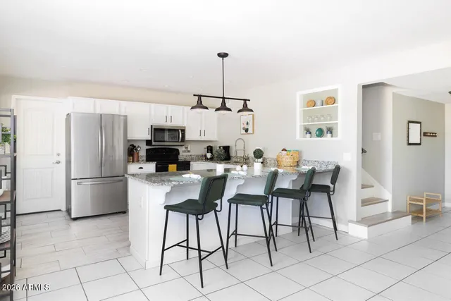 a kitchen with stainless steel appliances kitchen island granite countertop a refrigerator a stove a microwave oven with white cabinets and island