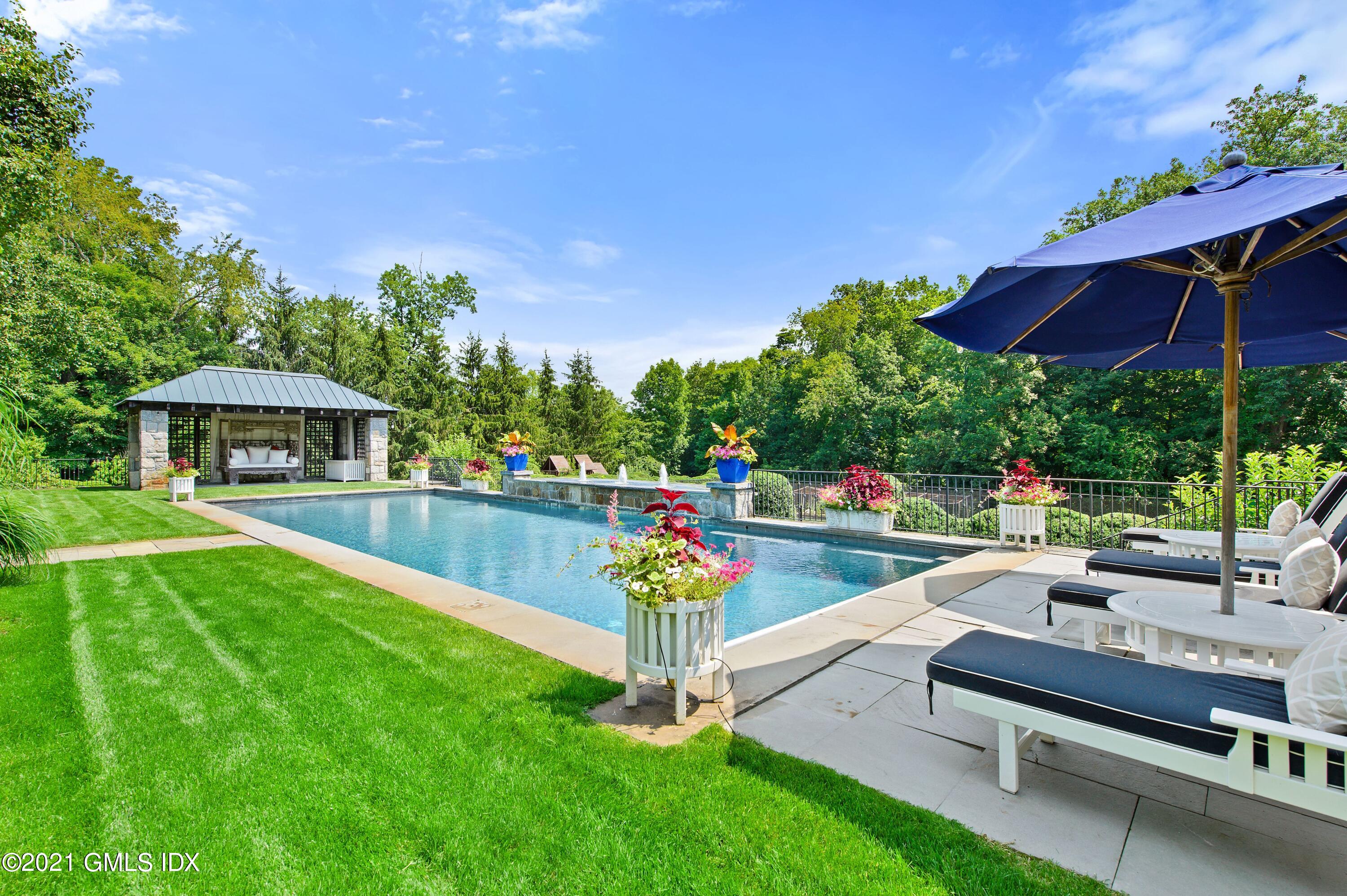 435 Round Hill Road Greenwich, CT 06831 - Photo 37 of 44 a view of a patio with couches table and chairs under an umbrella with palm trees