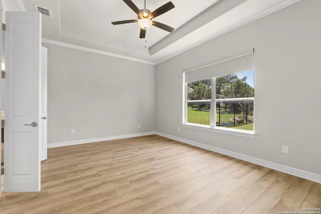 an empty room with wooden floor chandelier fan and windows