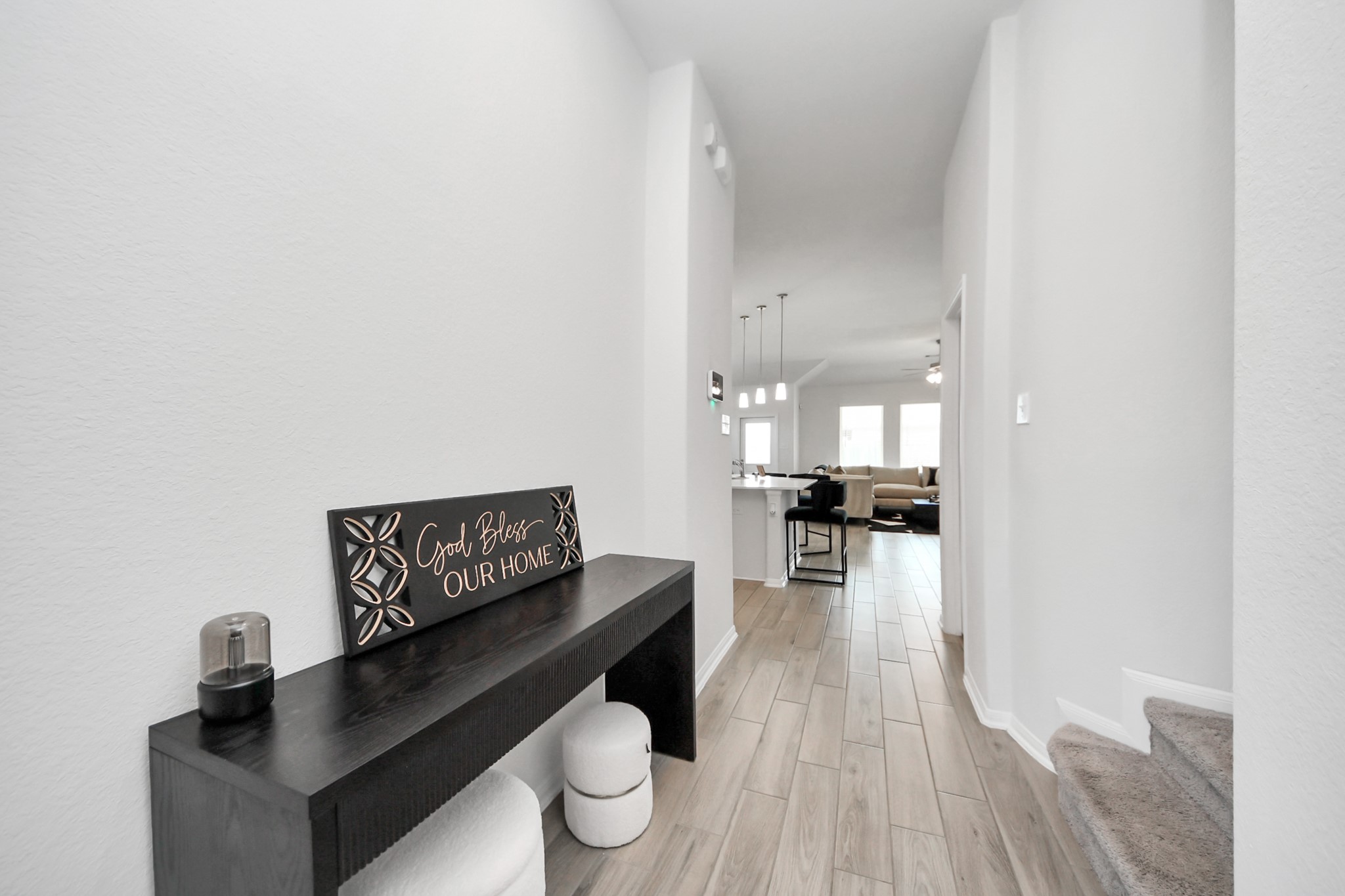 10603 Juniper Br Drive Rosharon, TX 77583 - Photo 12 of 50 This photo showcases a bright and welcoming entryway with light-colored walls and wood-look flooring. The hallway leads to an open-concept living area with a modern kitchen featuring a breakfast bar and pendant lighting. A cozy living space is visible in the background, offering a glimpse of comfort and style.