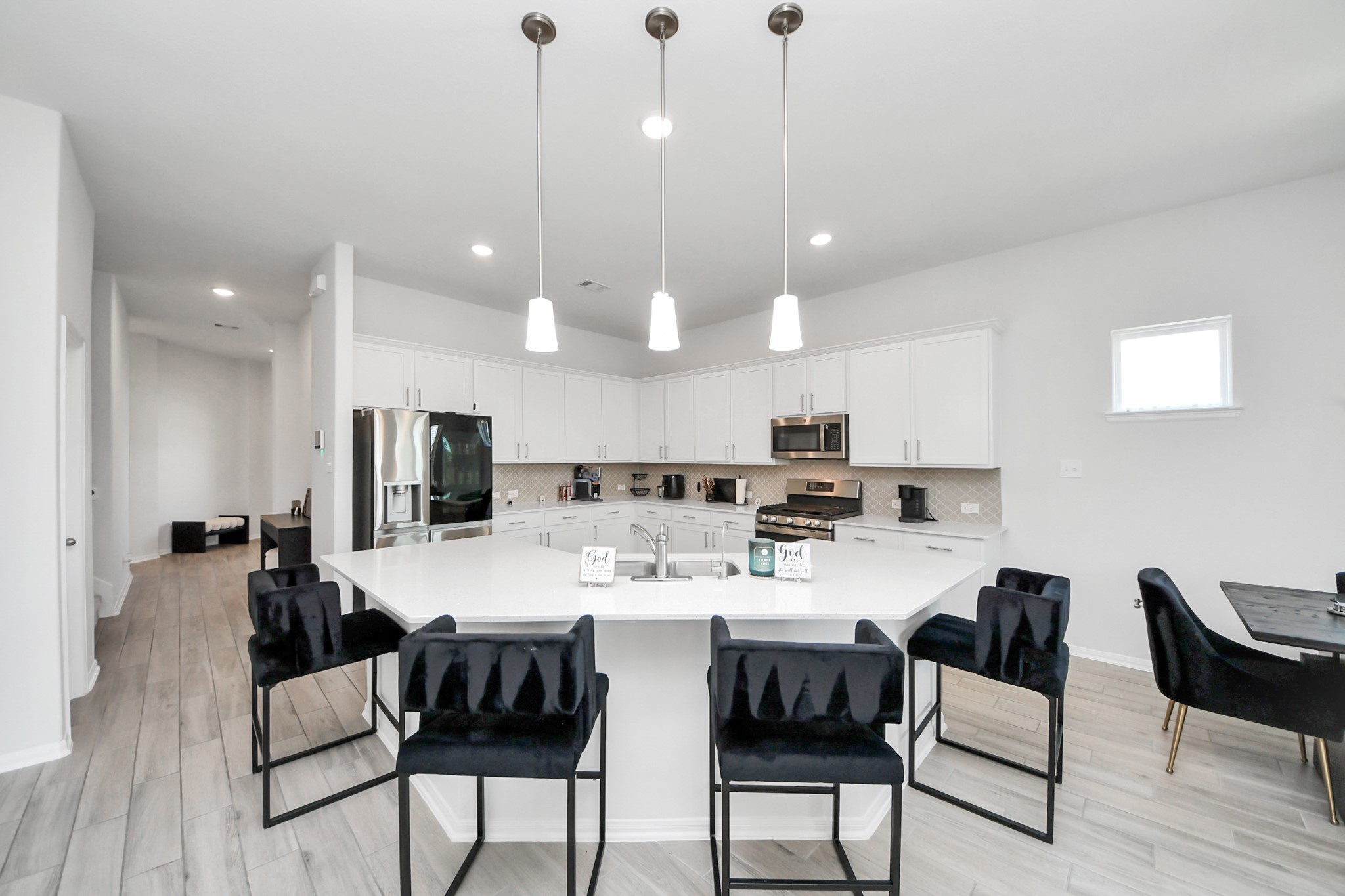 10603 Juniper Br Drive Rosharon, TX 77583 - Photo 13 of 50 This modern kitchen features a spacious layout with sleek white cabinetry, stainless steel appliances, and a large island with pendant lighting and seating for five. The open design is complemented by light wood flooring and ample natural light, creating an inviting space for cooking and entertaining.