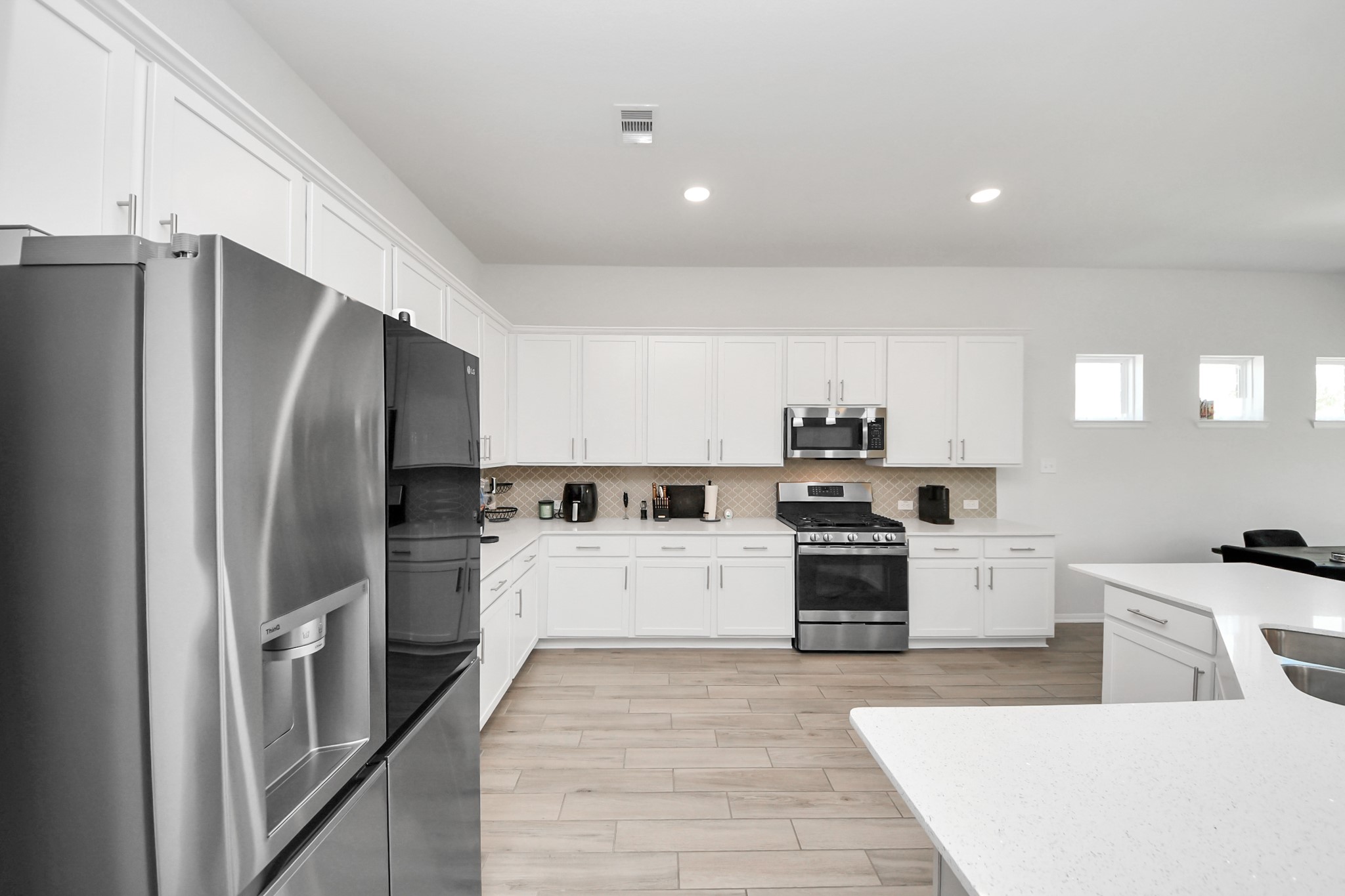 10603 Juniper Br Drive Rosharon, TX 77583 - Photo 14 of 50 Modern kitchen with stainless steel appliances, white cabinetry, and a spacious layout. It features a large refrigerator, gas stove, microwave, and ample counter space with a breakfast bar. Bright and open with natural light from small windows.