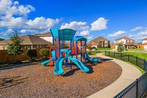 10603 Juniper Br Drive Rosharon, TX 77583 - Photo 49 of 50 This photo features a well-maintained playground with colorful slides, located in a residential neighborhood. The area is surrounded by neatly kept homes and a fence, offering a family-friendly environment with clear blue skies overhead.
