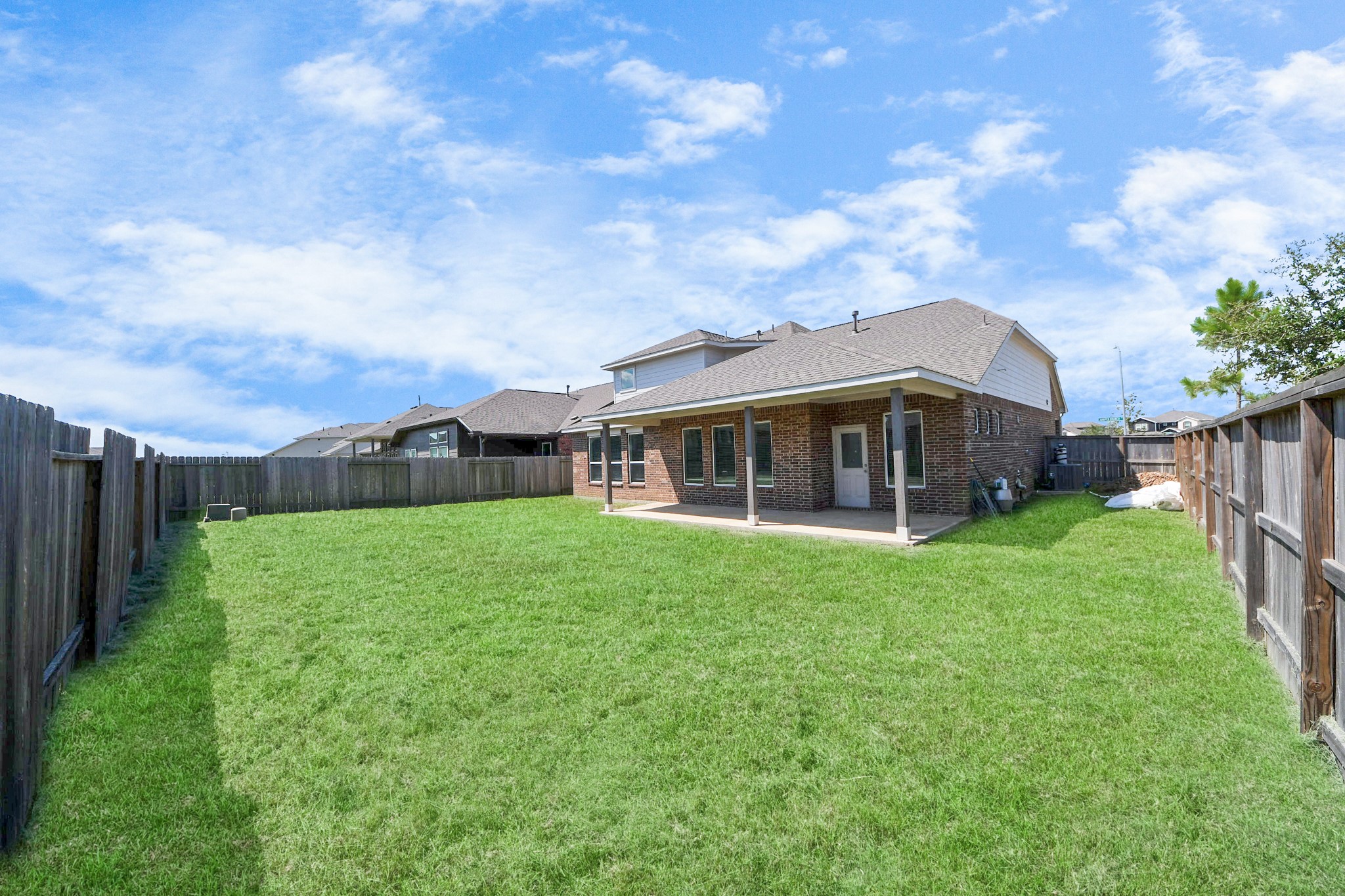 10603 Juniper Br Drive Rosharon, TX 77583 - Photo 5 of 50 Spacious backyard with lush green lawn, bordered by wooden fencing. Features a covered patio attached to a brick house, perfect for outdoor activities and relaxation.