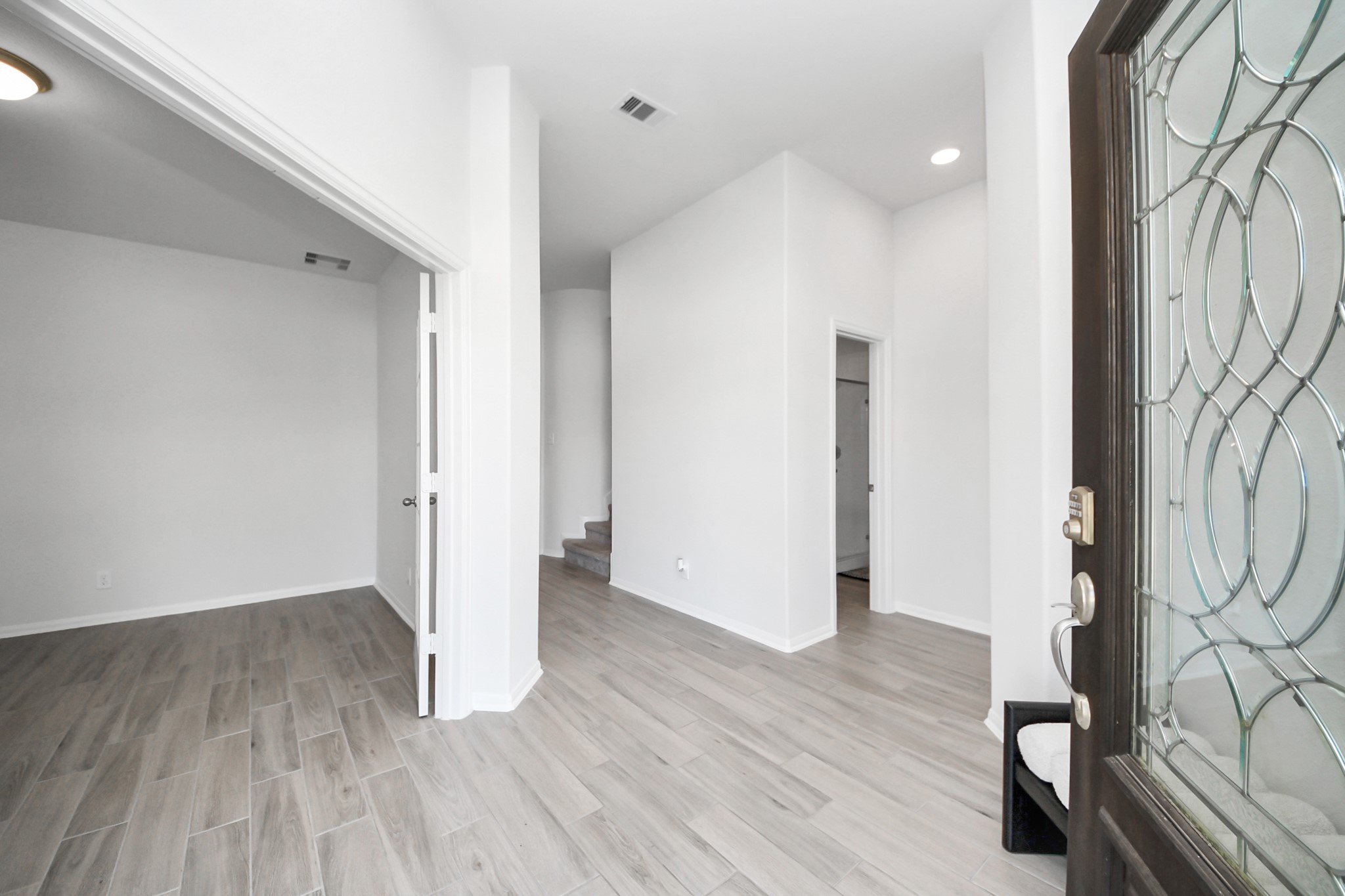 10603 Juniper Br Drive Rosharon, TX 77583 - Photo 7 of 50 This photo shows a bright, open entryway with light wood flooring and white walls. A decorative glass front door allows natural light to enter. The hallway leads to additional rooms and a staircase, providing a welcoming and spacious feel.
