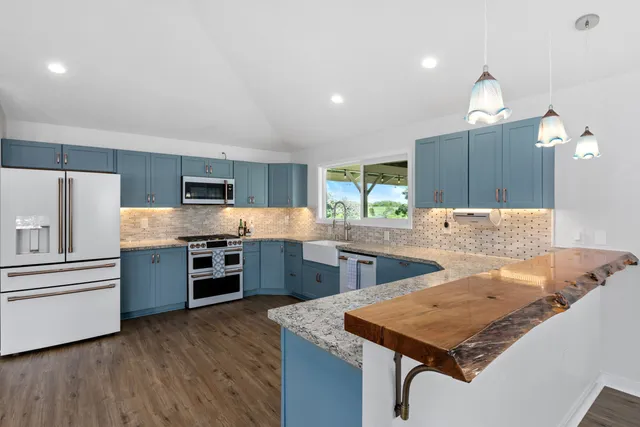 a kitchen with stainless steel appliances kitchen island granite countertop a refrigerator a stove top oven a sink dishwasher and wooden cabinets with wooden floor