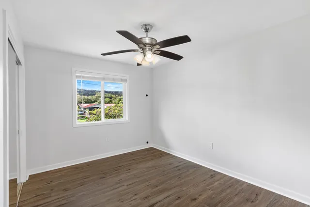 an empty room with wooden floor ceiling fan and windows