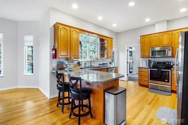a kitchen with stainless steel appliances granite countertop a stove top oven a sink dishwasher and chairs with wooden floor