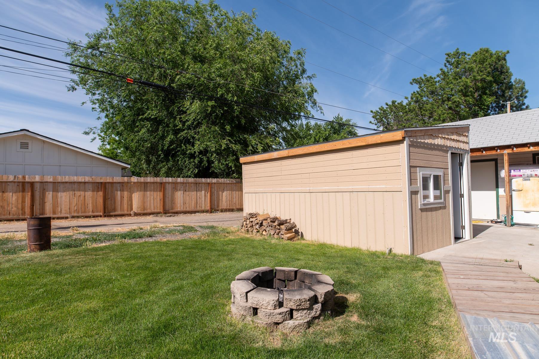 736 East Main Street Weiser, ID 83672 - Photo 33 of 33 Expansive backyard featuring a stone fire pit, wood privacy fencing, and a separate storage shed with an awning