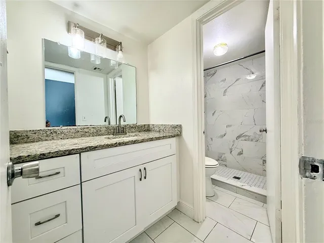 a bathroom with a granite countertop sink a mirror a bathtub and shower