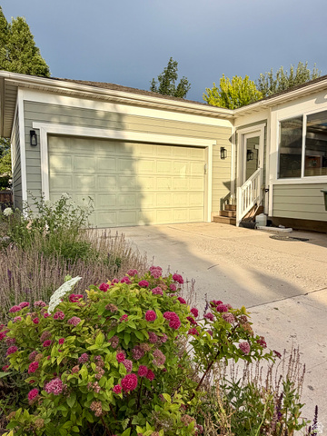 11751 Lake Run Road South Jordan, UT 84009 - Photo 37 of 38 Attached garage with a panel door, light green siding, and exterior wall sconces, complemented by a concrete driveway and mature landscaping with flowering shrubs