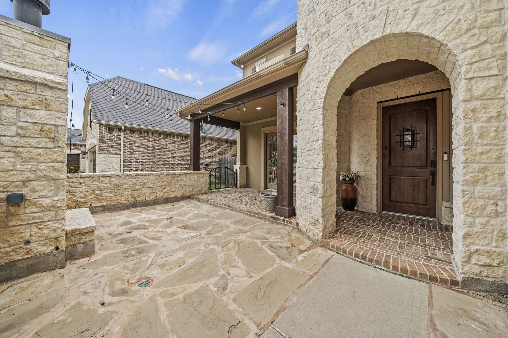 14215 Spindle Arbor Road Cypress, TX 77429 - Photo 8 of 47 This photo showcases a welcoming stone entryway with a rustic wooden door and a covered patio area. The charming courtyard features stone paving and string lights, providing a cozy and inviting atmosphere.