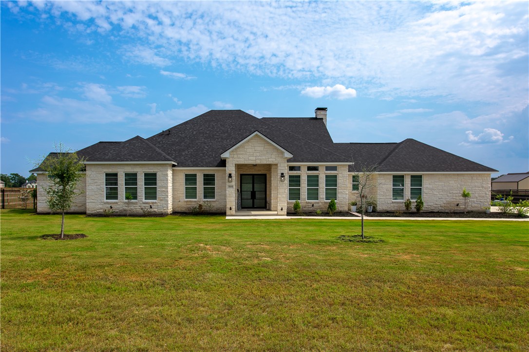 View of front facade featuring stone siding, a front lawn, and roof with shingles