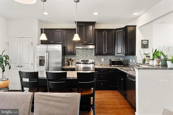 a kitchen with stainless steel appliances granite countertop a refrigerator a sink a stove a dining table and chairs