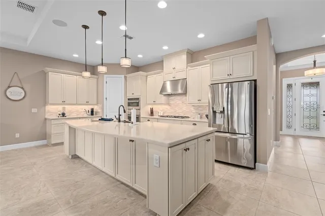 a large white kitchen with a large island oven a stove a sink a dining table and chairs with wooden floor