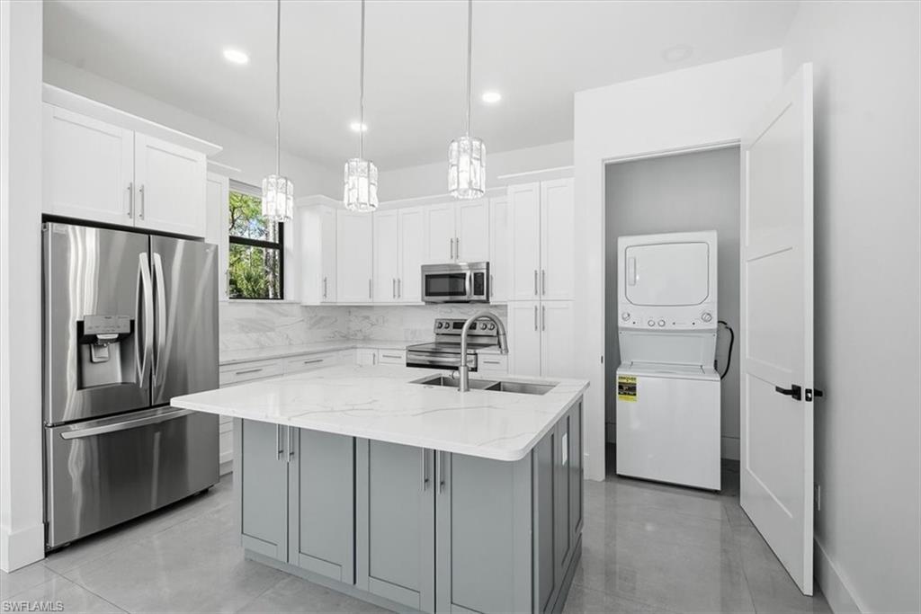 3261 15th Avenue Southwest Naples, FL 34117 - Photo 7 of 20 Kitchen with appliances with stainless steel finishes, white cabinets, a kitchen island with sink, stacked washer / dryer, and light stone counters
