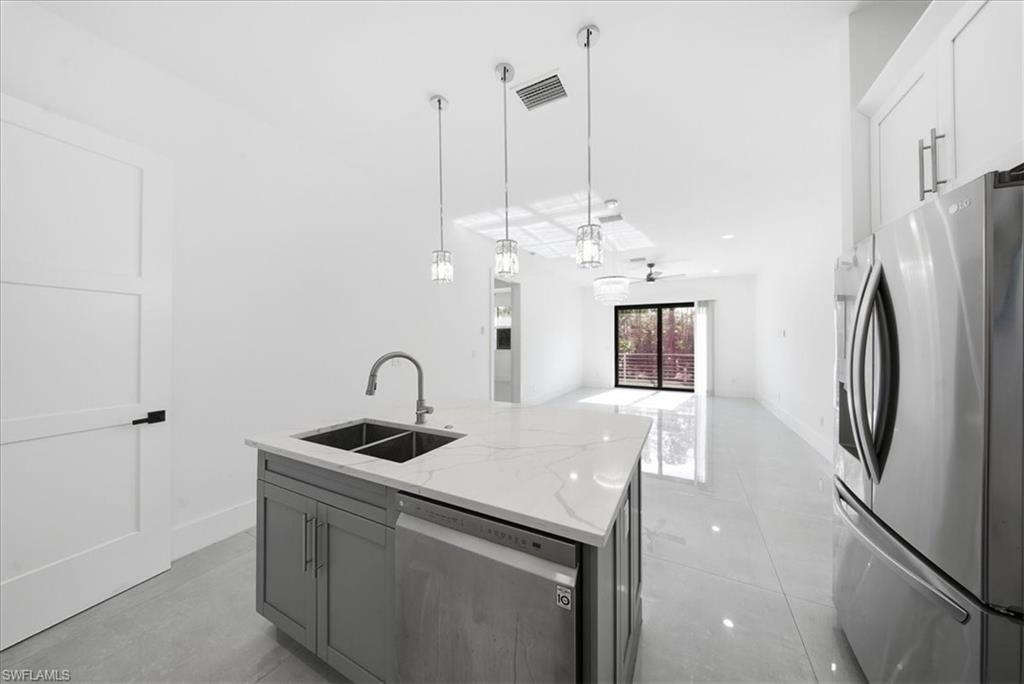 3261 15th Avenue Southwest Naples, FL 34117 - Photo 20 of 20 Kitchen featuring appliances with stainless steel finishes, light stone countertops, hanging light fixtures, a center island with sink, and open floor plan