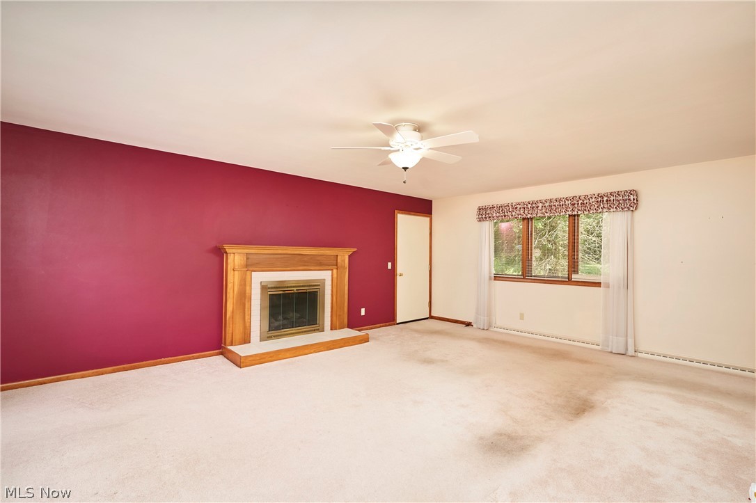 299 West Caston Road New Franklin, OH 44319 - Photo 8 of 23 Spacious room featuring a wood-surround fireplace with a hearth, triple window unit, white ceiling fan, and light-toned carpet flooring