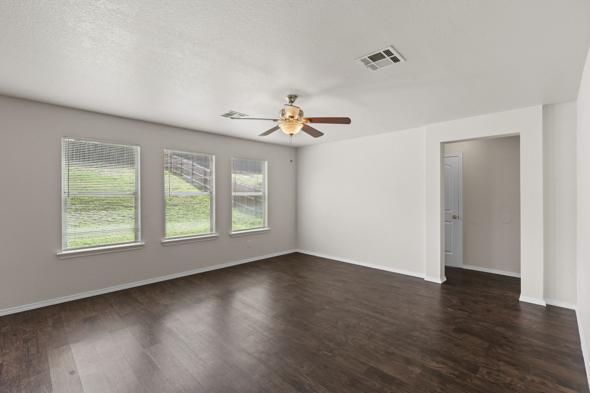208 Dandelion Loop Kyle, TX 78640 - Photo 17 of 39 Living area featuring dark wood flooring, light-colored walls, a ceiling fan with integrated lighting, and three windows offering views of green space