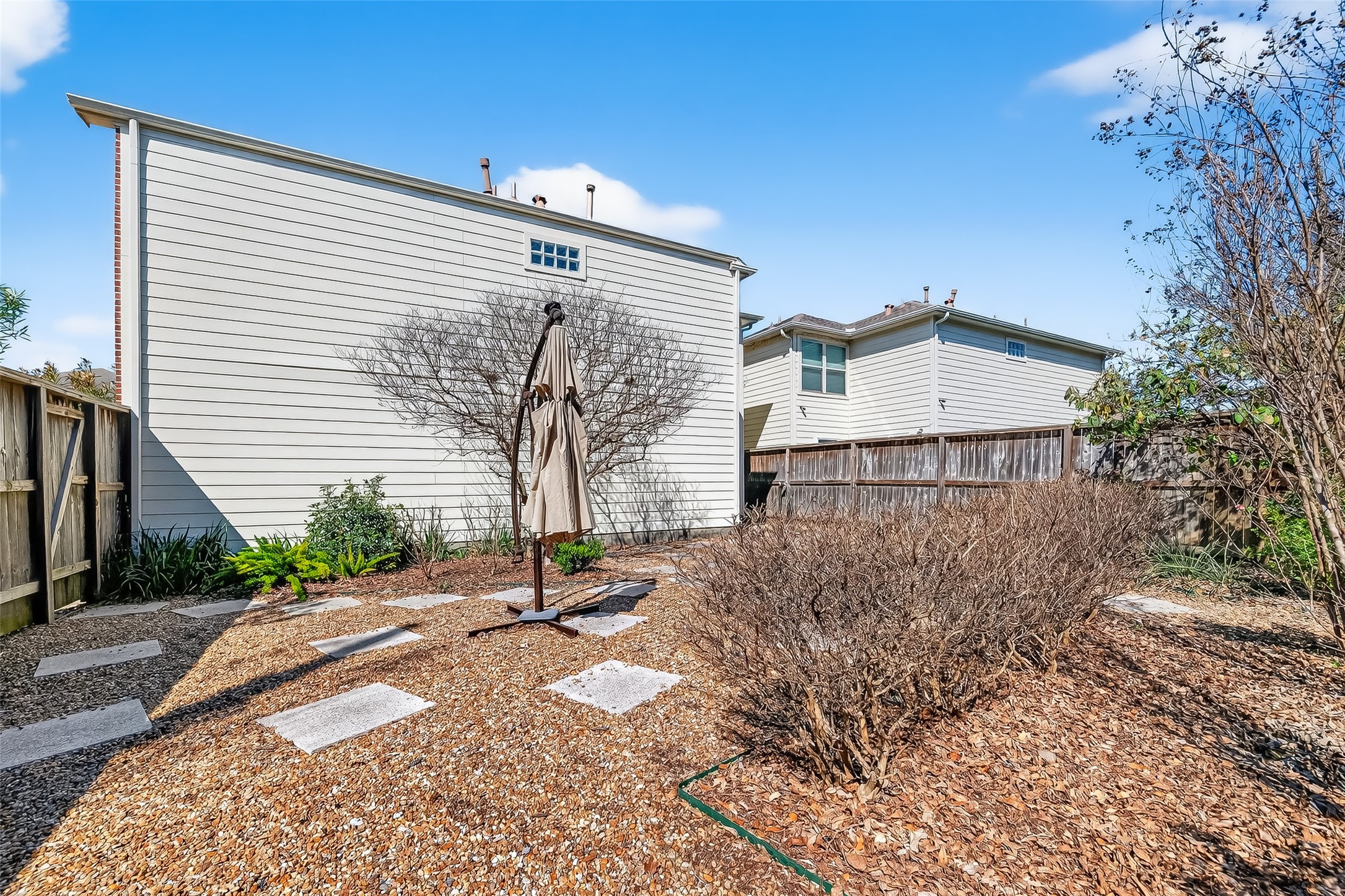 5951 S Loop East, Unit 47 Houston, TX 77033 - Photo 31 of 37 A cozy backyard with low-maintenance landscaping, featuring gravel and stepping stones. There's a central patio umbrella for shade, surrounded by some shrubs and a wooden fence for privacy. Ideal for relaxing outdoors.