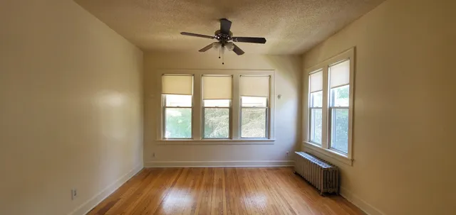 an empty room with wooden floor fan and windows