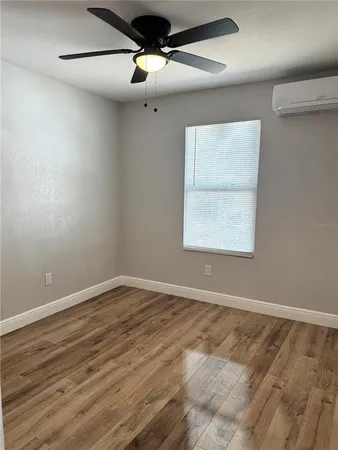 an empty room with wooden floor chandelier fan and windows