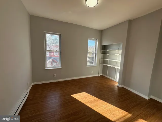 an empty room with wooden floor closet and windows