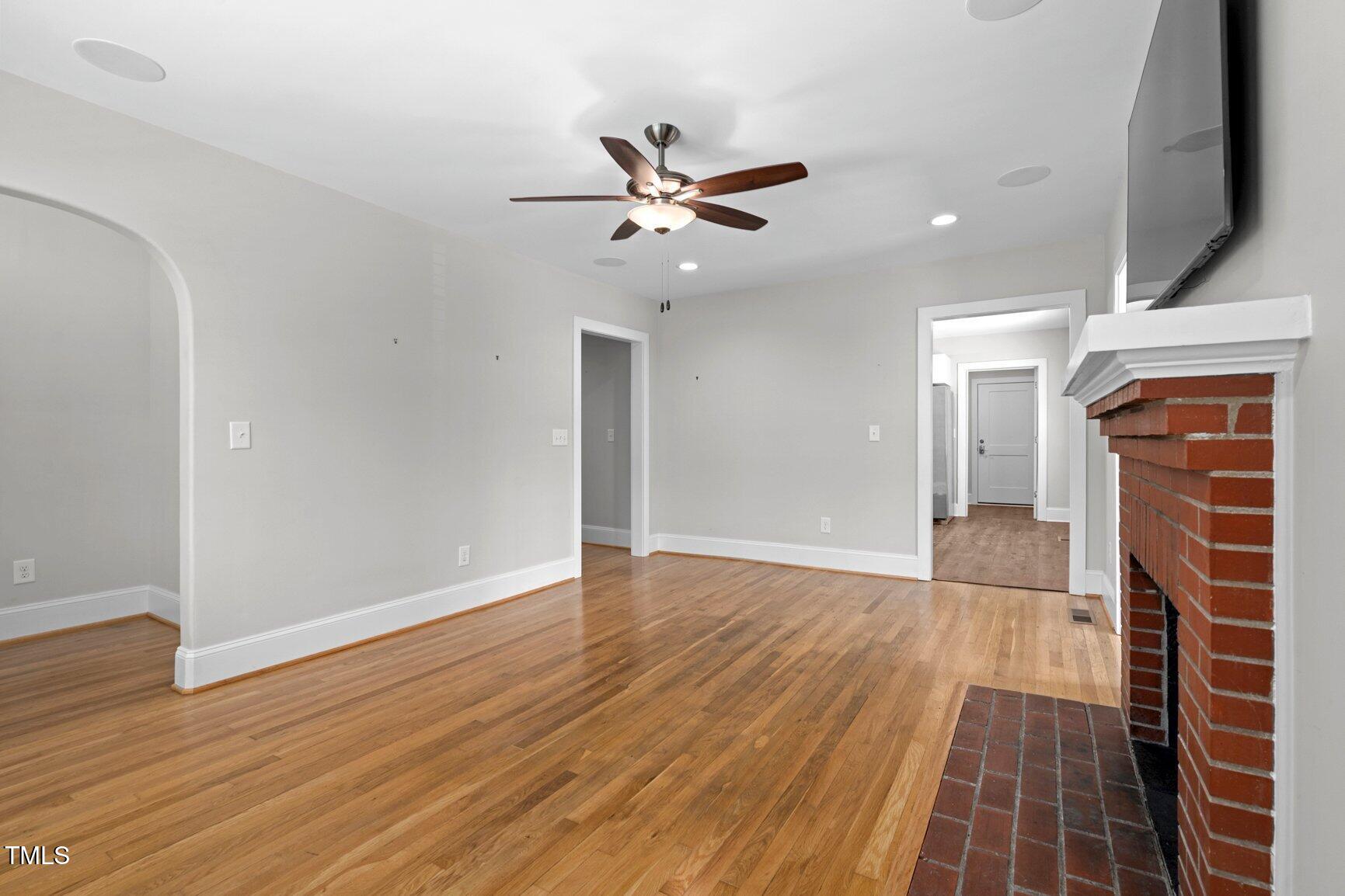 216 Whitfield Street Enfield, NC 27823 - Photo 7 of 31 an empty room with wooden floor a ceiling fan a fireplace and windows