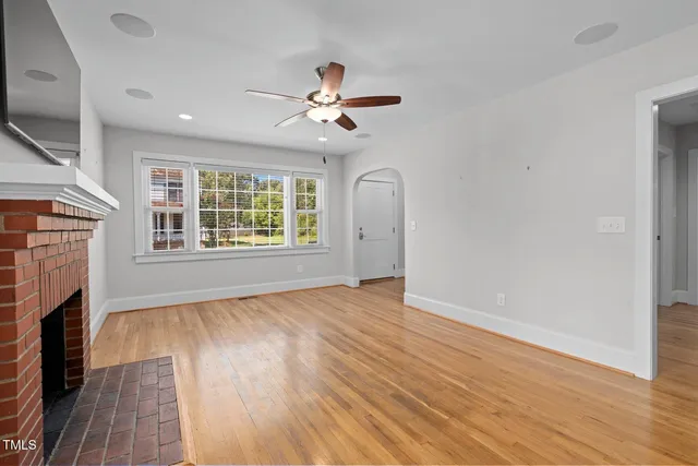 an empty room with wooden floor a ceiling fan a fireplace and windows