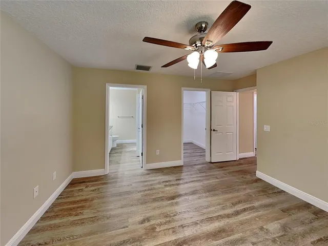 a view of an empty room with wooden floor and a ceiling fan