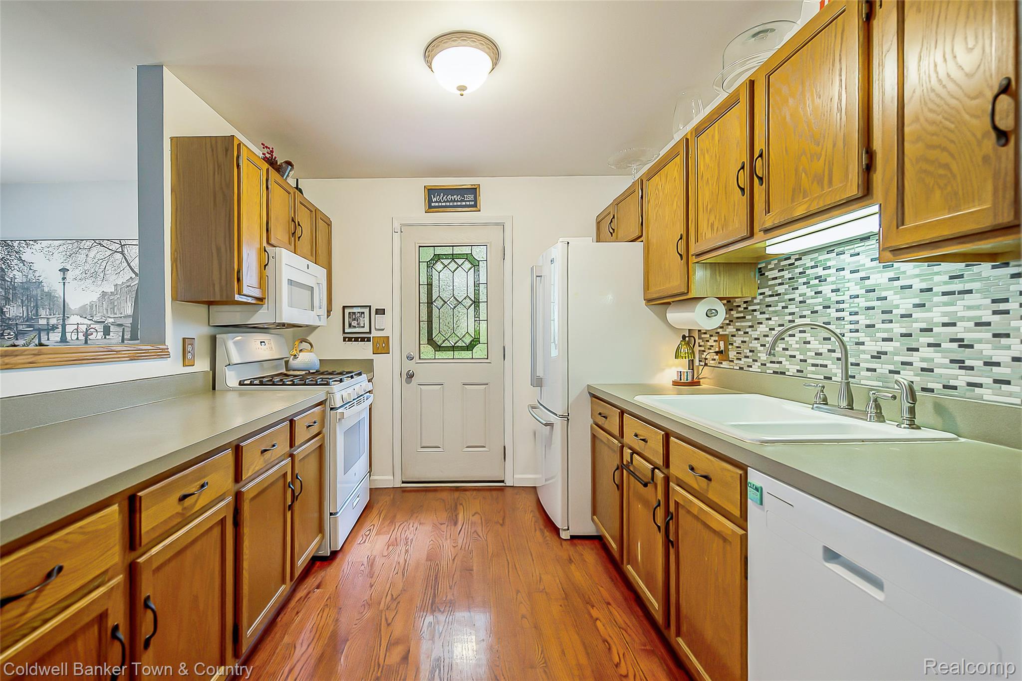 411 Springwell Lane Howell, MI 48843 - Photo 10 of 33 Galley kitchen featuring wood-finish flooring, light wood cabinetry, white appliances, and a mosaic tile backsplash