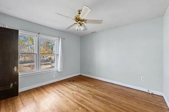 an empty room with wooden floor fan and windows