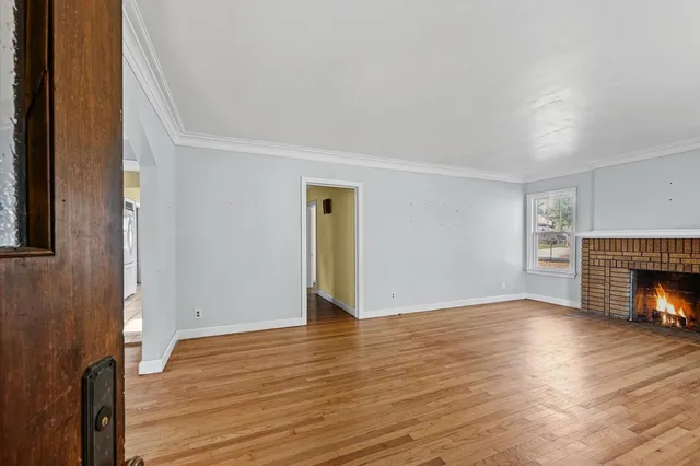a view of an empty room with wooden floor fireplace and a window