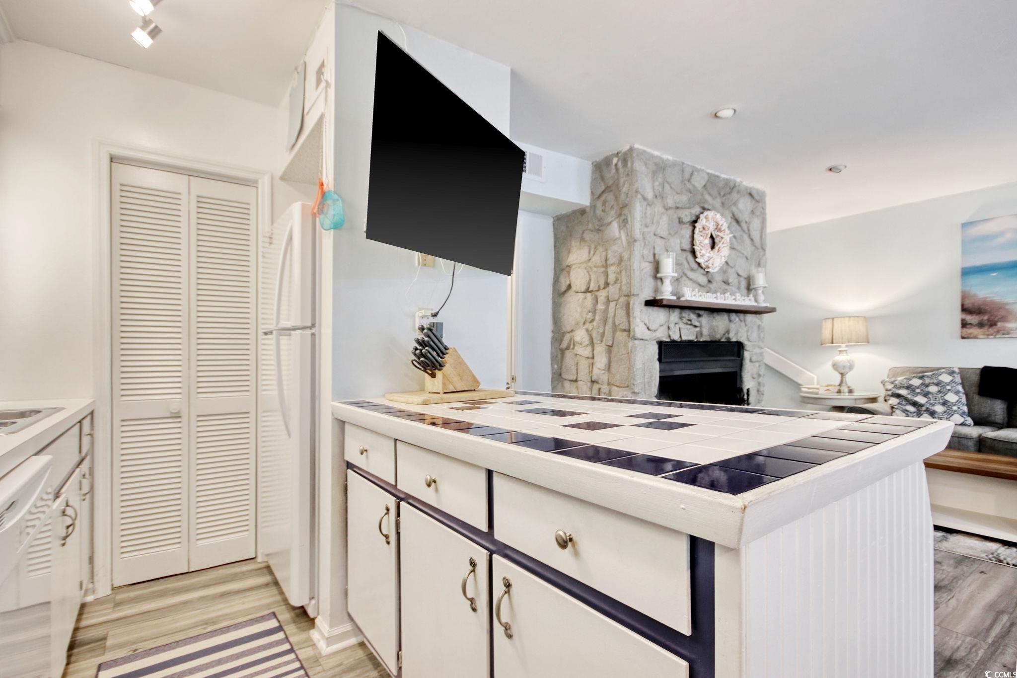 Kitchen featuring white cabinetry, tile countertops, white appliances, a fireplace, and light wood-style flooring