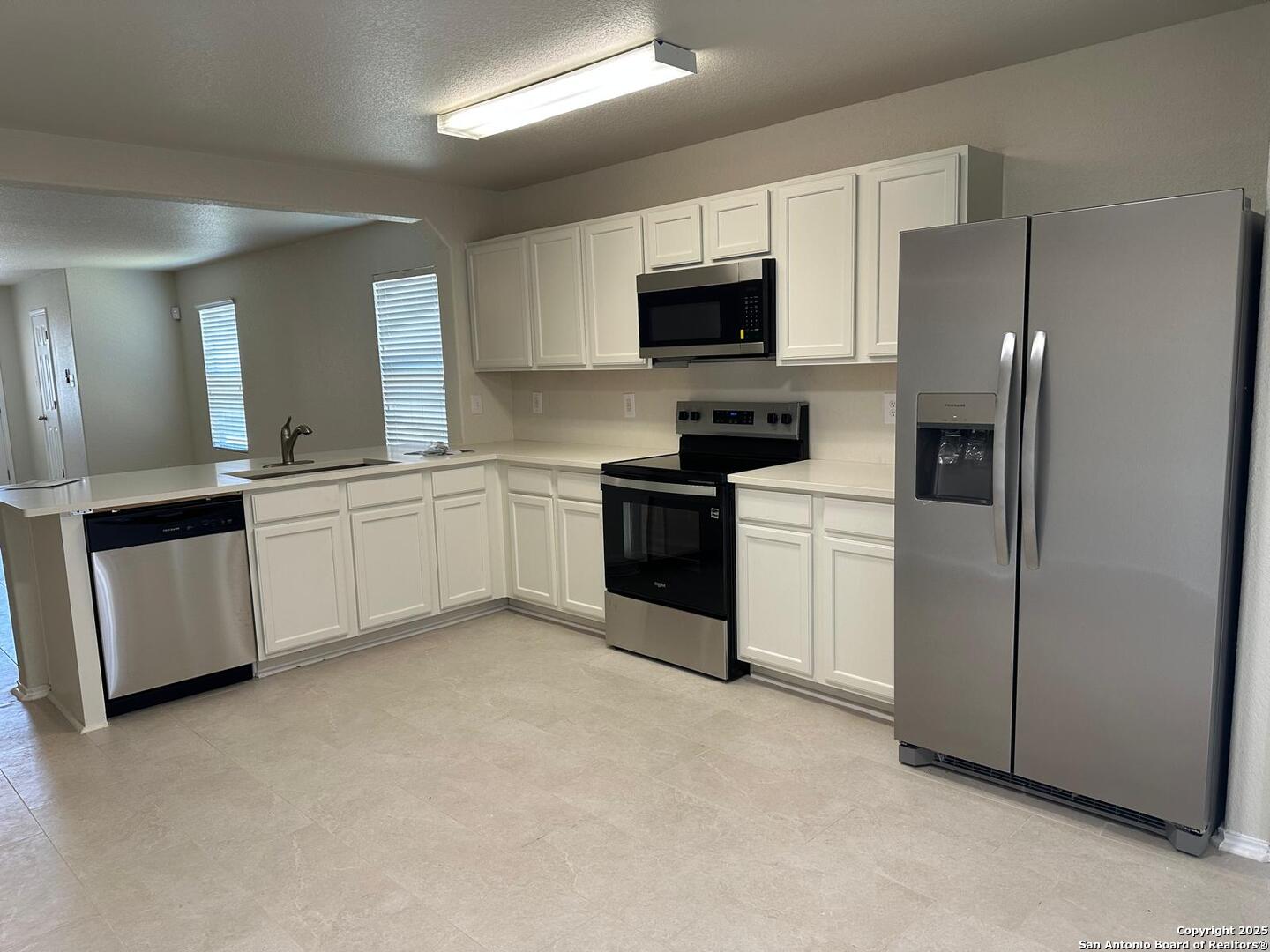 a kitchen with stainless steel appliances granite countertop white cabinets a sink a stove a microwave a refrigerator a sink and white cabinets