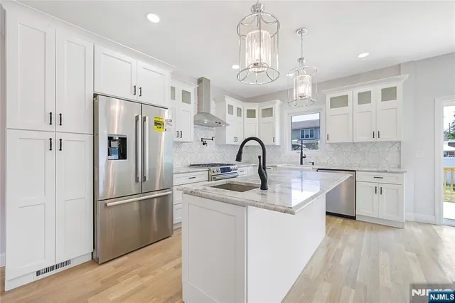 a kitchen with stainless steel appliances granite countertop a refrigerator a sink dishwasher a stove and a dining table with wooden floor