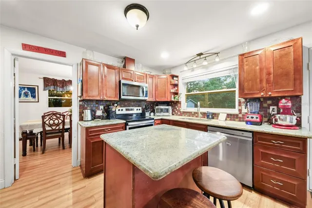 a kitchen with stainless steel appliances granite countertop a stove top oven a sink dishwasher a dining table and chairs with wooden floor