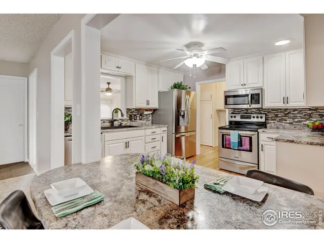 a kitchen with stainless steel appliances kitchen island granite countertop a refrigerator oven stove a sink a dining table and chairs with wooden floor