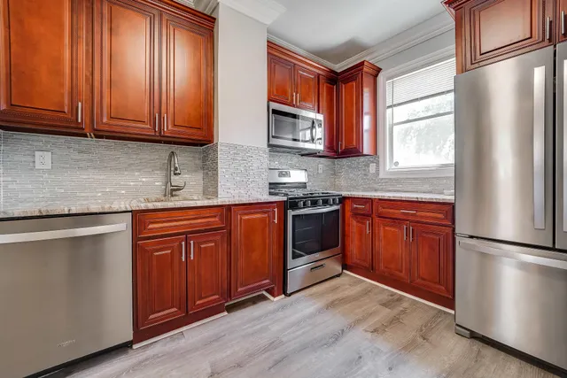 a kitchen with stainless steel appliances granite countertop a refrigerator a sink dishwasher a stove with wooden cabinets and floor