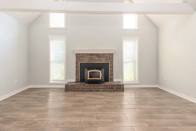 a view of an empty room with wooden floor fireplace and a window